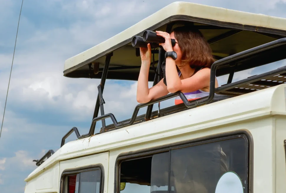 A tourist watching birds with a binoculars aboard a Likana Safaris Landcruiser