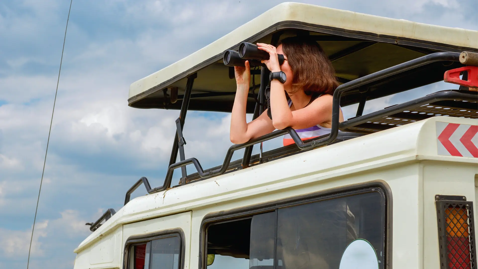 A tourist watching birds with a binoculars aboard a Likana Safaris Landcruiser